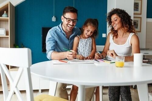 Smiling man, girl and woman sitting around a table coloring.