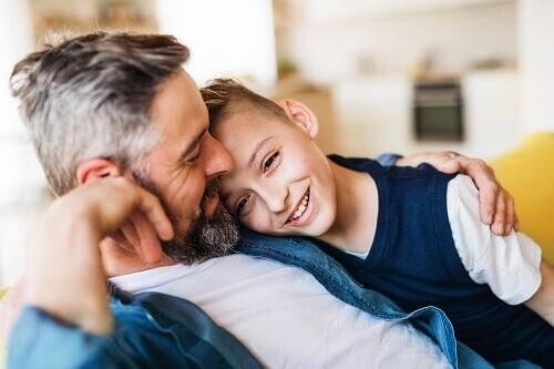 Smiling man sitting with his arm around a young smiling boy.